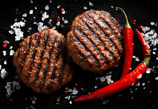 Gegrillte Burgerpatties mit Chili und Salz auf schwarzem Hintergrund
