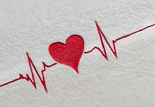 Rotes geprägtes Herz mit EKG Linie auf strukturiertem Papier