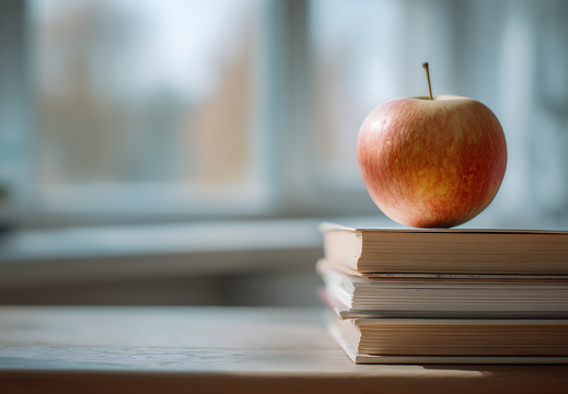 Apfel auf Bücherstapel vor Fenster im Klassenzimmer