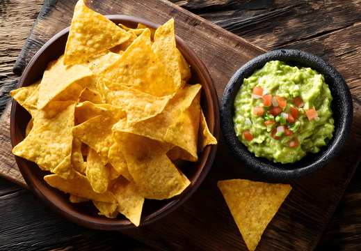 Nachos mit Guacamole in schwarzer Schale auf rustikalem Brett